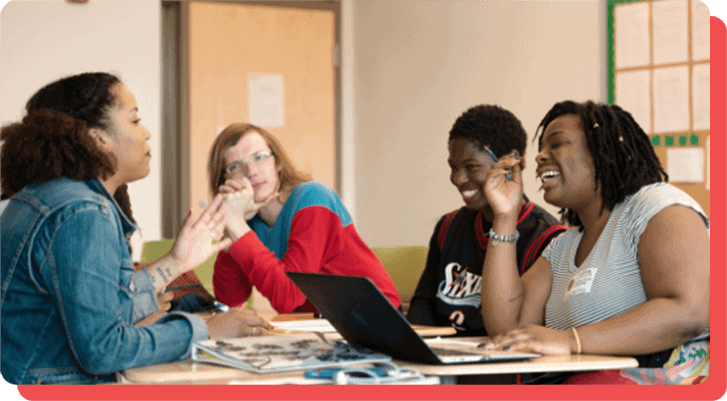 Youth and mentors sit together around a table laughing.