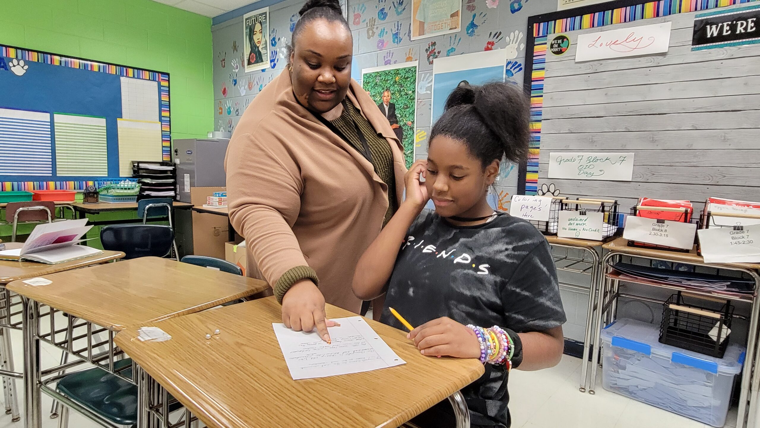 A mentor instructs a student while pointing at their paper. The student look focuses on the instruction.