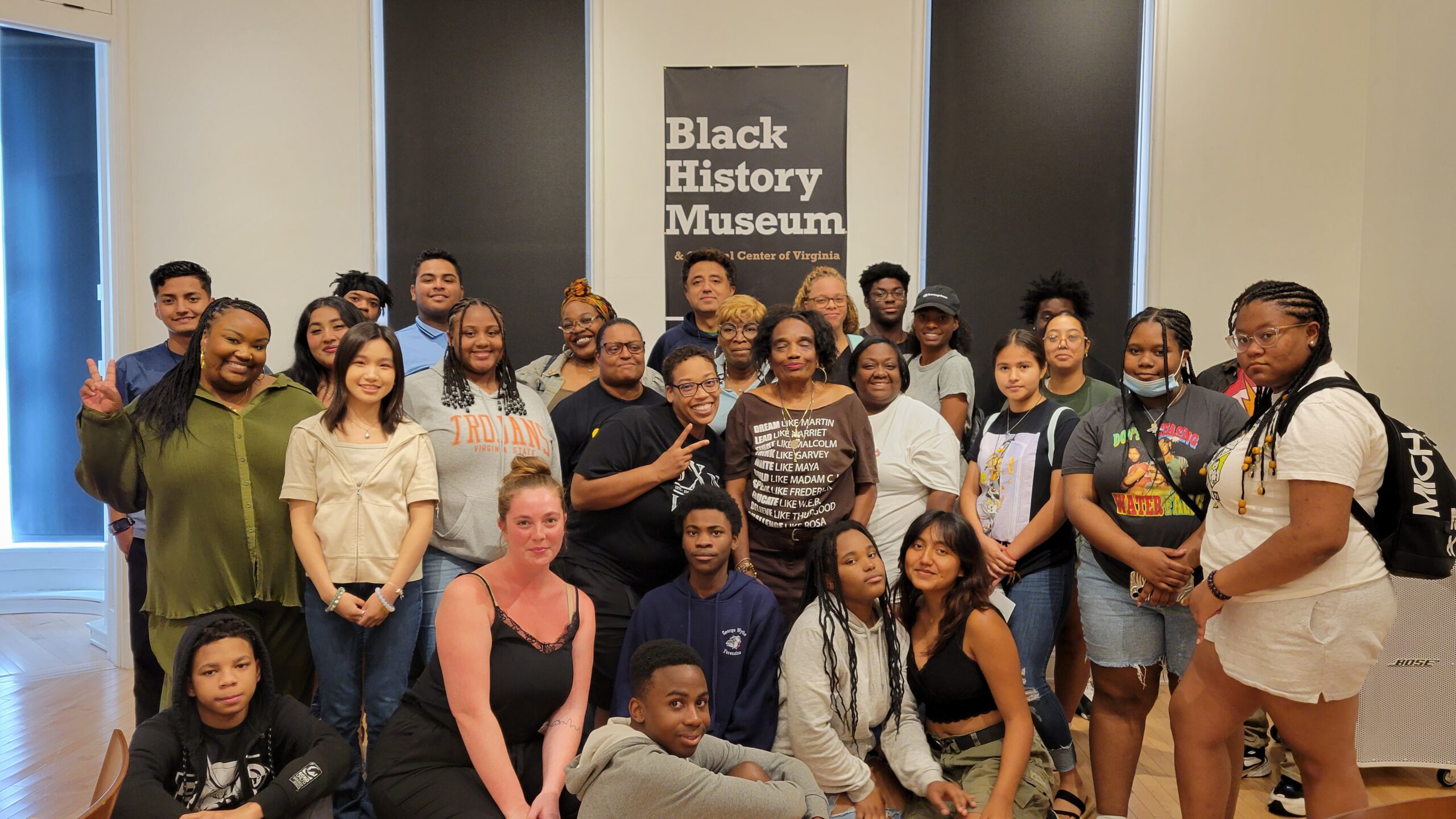 Several youth, mentors, and teachers pose for a group shot in front of a sign that reads "Black History Museum".